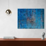 Layered and glowing abstract landscape in orange and blueposter format displayed in a grey wall, brown desk