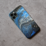 Phone case displayed on a grey concrete surface featuring the artwork “Rome”, a fluid blue, white, and black abstract painting.