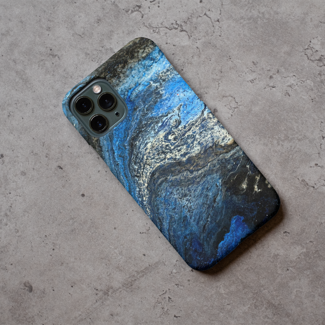 Phone case displayed on a grey concrete surface featuring the artwork “Rome”, a fluid blue, white, and black abstract painting.