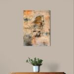 Abstract art poster with hidden face and warm layered colors behind wooden cabinet with small potted plant